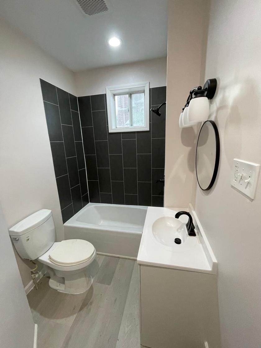 Remodeled bathroom with charcoal wall panels around the tub, a white vanity and black fixtures