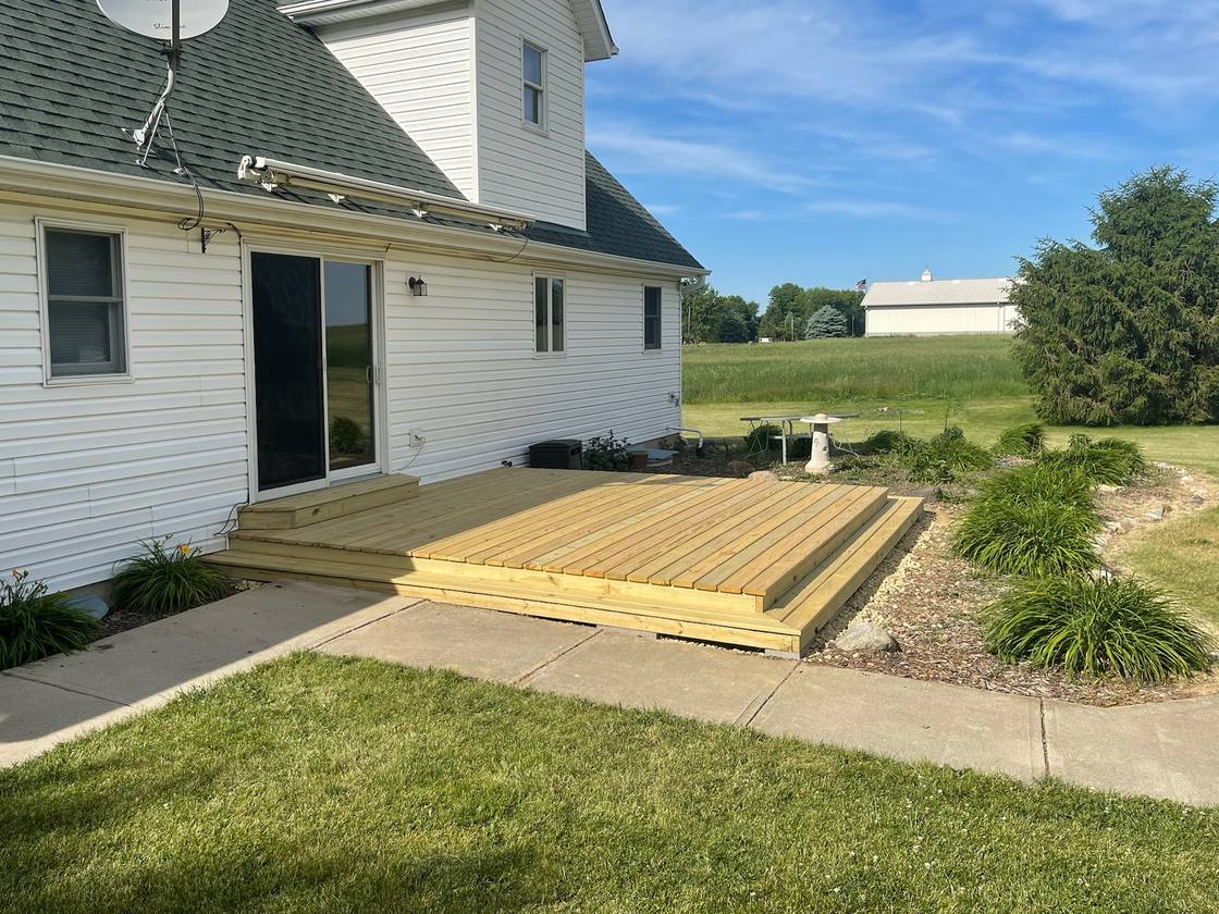 Ground-level wood deck with a wraparound step behind a white farmhouse